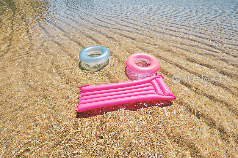 6月的一个完美的日子里，康沃尔的Pedn Vounder海滩，在清澈的浅海中，两个橡皮环和一个气垫排成一个笑脸形状。